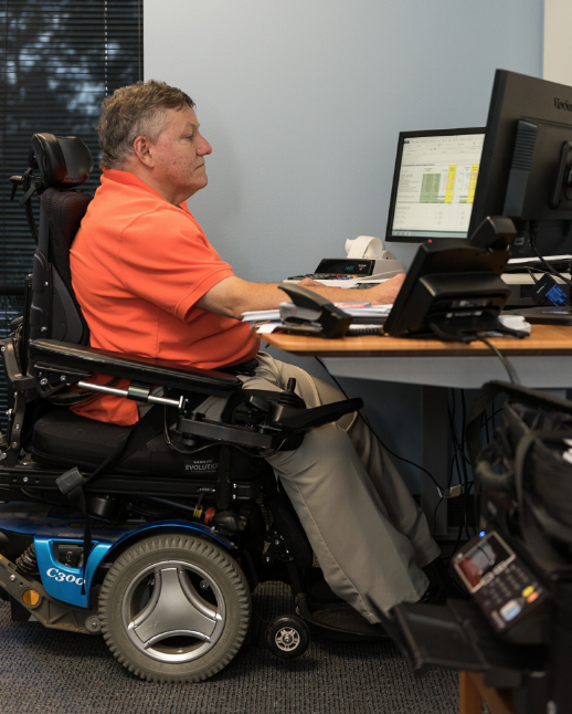 Professional CPA in a wheelchair working.  He has two large screens and a raised desk to make his workstation more accessible.