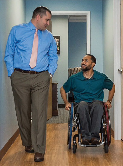 Man walking side-by-side with man in wheelchair discussing an issue.