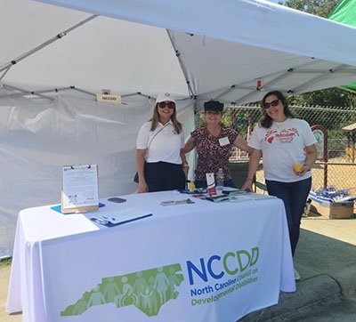 Irlanda Ruiz standing with two others at a table at an outdoor cultural celebration event.